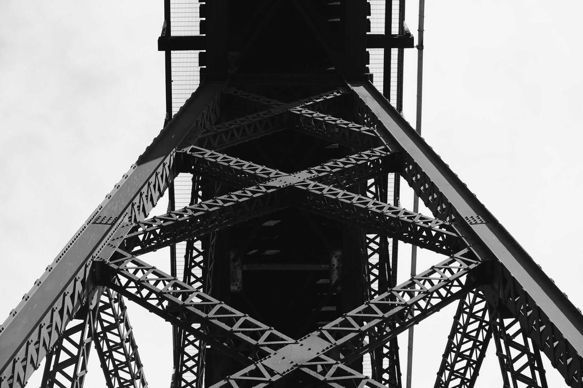 Чёрно-белая фотография стального моста снизу.